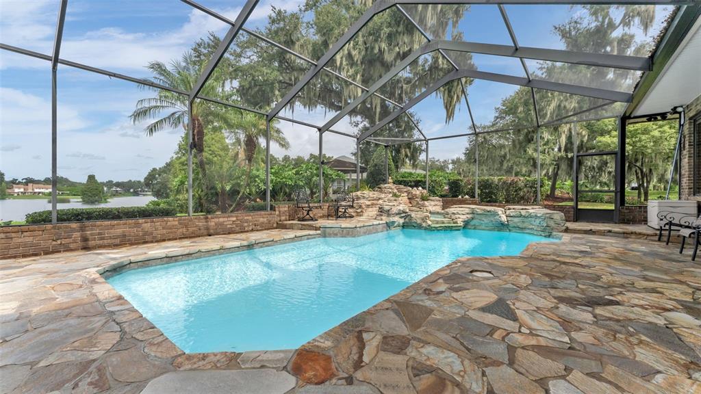 A screened-in swimming pool with a rock waterfall feature and stone patio overlooking a lake — 148 E CHRISTINA BOULEVARD, LAKELAND, FL
