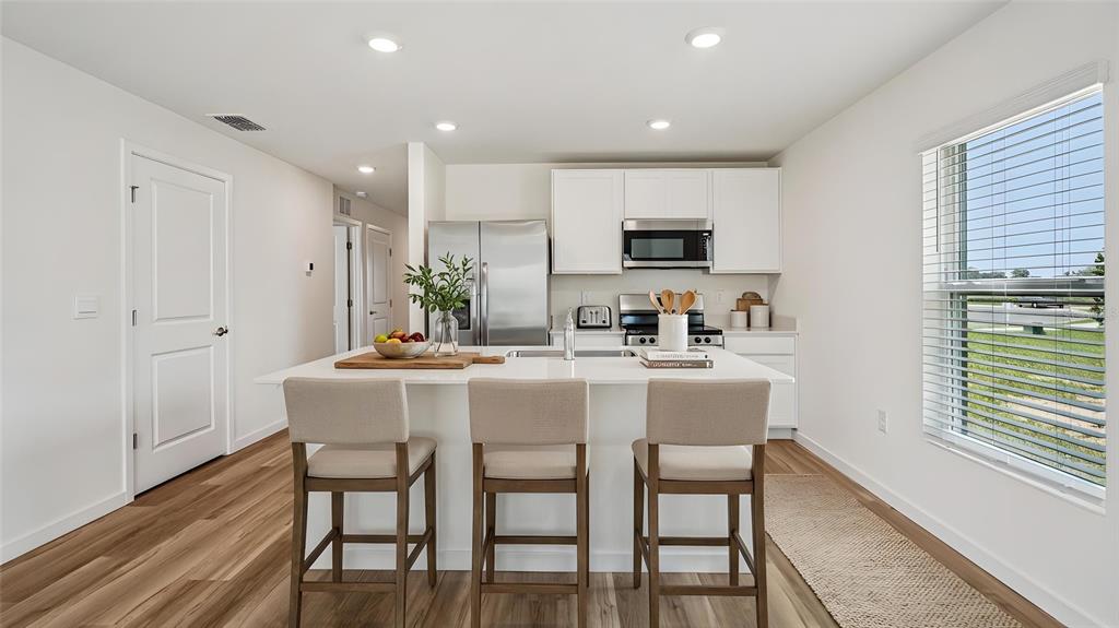 A modern kitchen features a white island with bar stools, stainless appliances, and wood flooring — 4129 KONA CIRCLE, SPRING HILL, FL