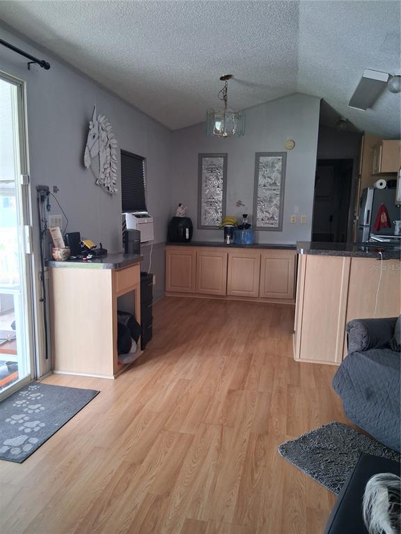 A kitchen and living area with light wood cabinets, laminate flooring, and a sliding door — 1359 SHIPWRECK LANE, ST CLOUD, FL