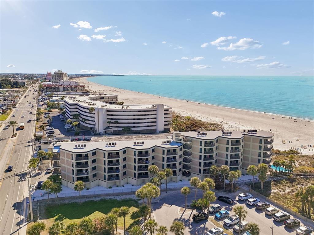 An aerial view shows a multi-story beachfront condominium complex next to a road and beach — 4510 GULF BOULEVARD UNIT 308, ST PETE BEACH, FL