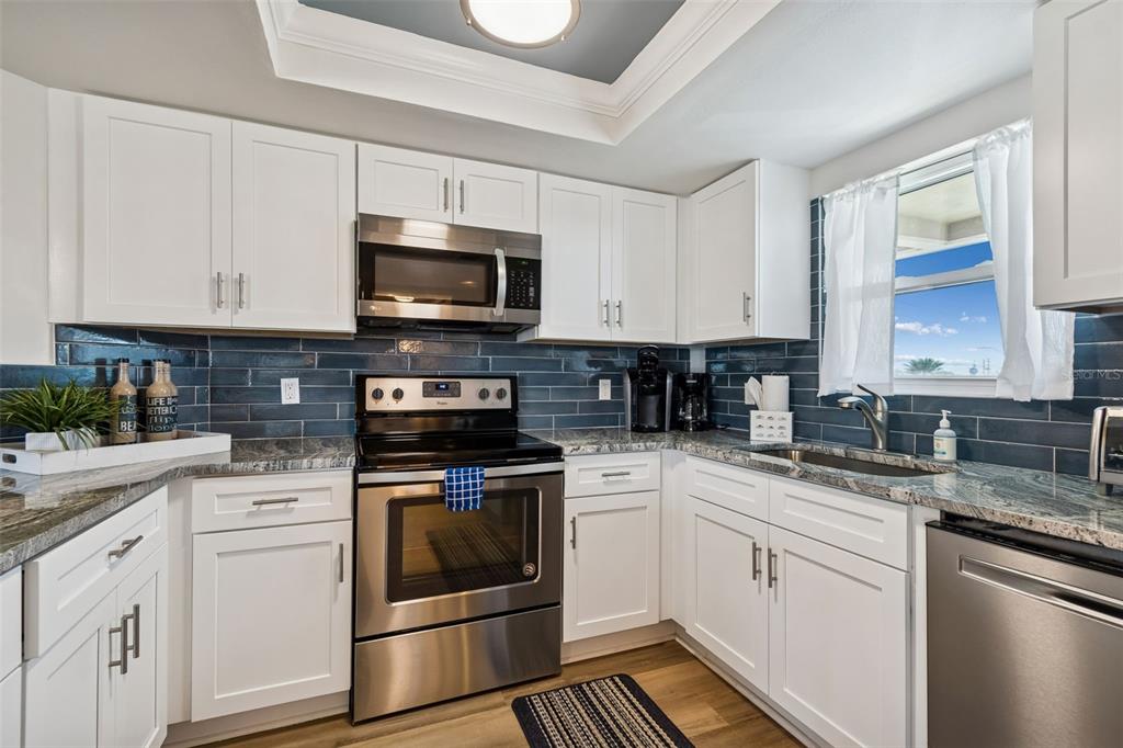 A kitchen with white cabinets, stainless steel appliances, granite countertops, and blue subway tile backsplash — 4510 GULF BOULEVARD UNIT 308, ST PETE BEACH, FL