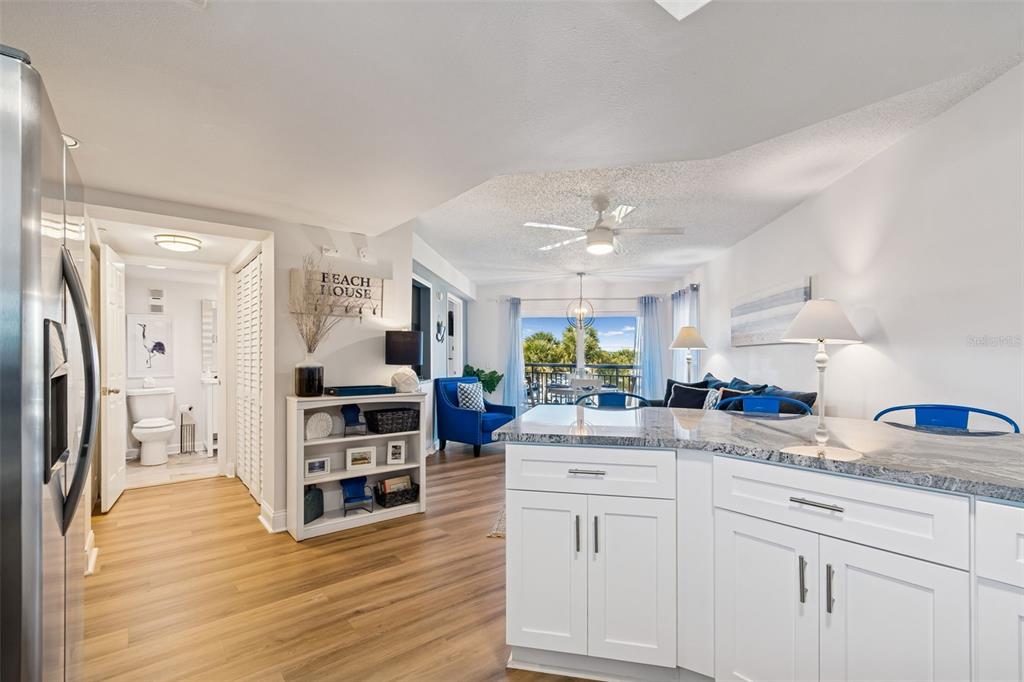 A kitchen island with granite countertops overlooks a living area with wood-look flooring and balcony — 4510 GULF BOULEVARD UNIT 308, ST PETE BEACH, FL