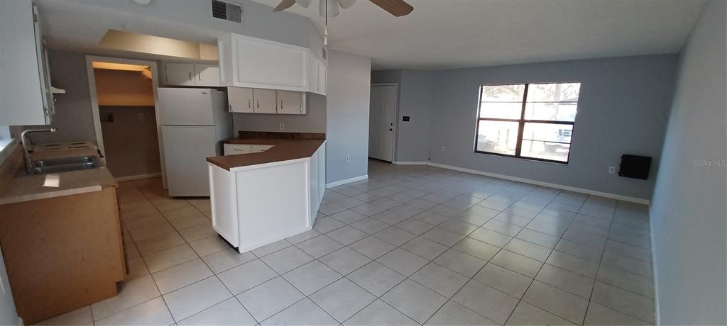 An open-concept kitchen and living area with white cabinets, brown countertops, and light tile flooring — 6120 GEORGIA AVENUE, NEW PORT RICHEY, FL
