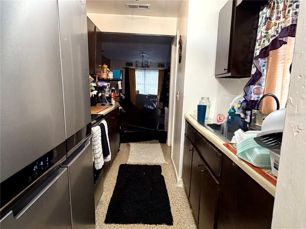 A narrow galley kitchen features dark wood cabinets, stainless steel appliances, and a double sink — 1499 AVENUE E NE, WINTER HAVEN, FL