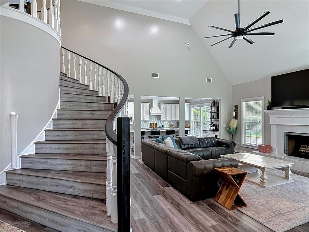 A living room features a curved staircase, vaulted ceilings, and a dark leather sectional sofa — 38 WINDING CREEK WAY, ORMOND BEACH, FL