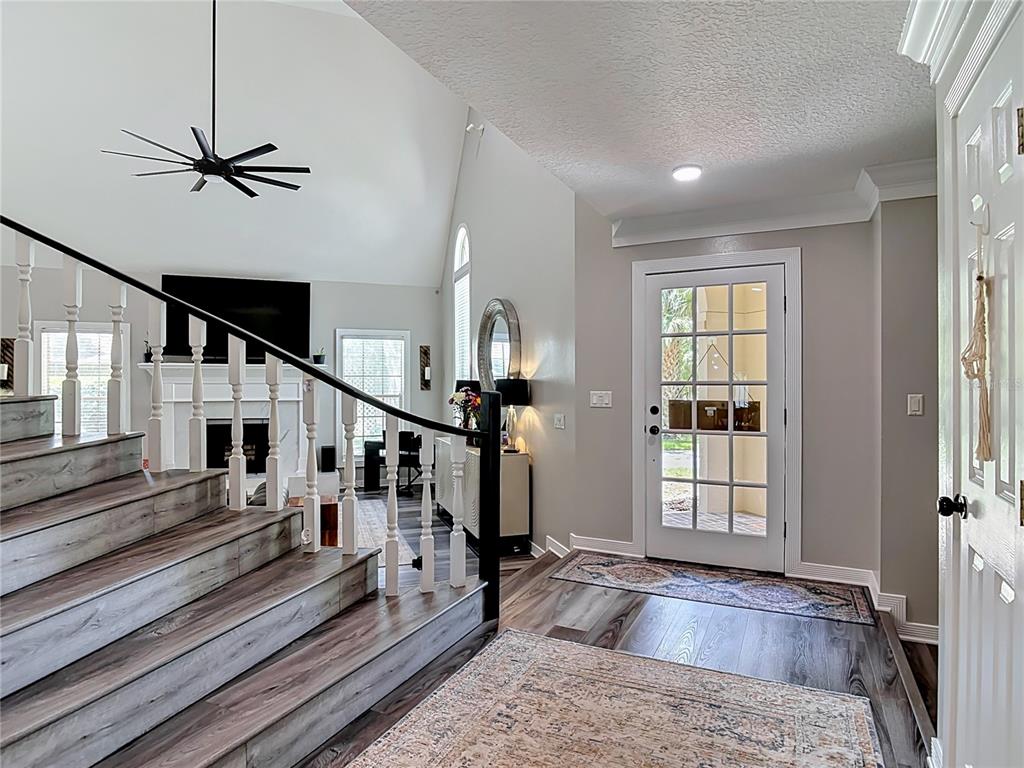 A foyer with wood-look flooring leads to a staircase and a living room with vaulted ceilings — 38 WINDING CREEK WAY, ORMOND BEACH, FL