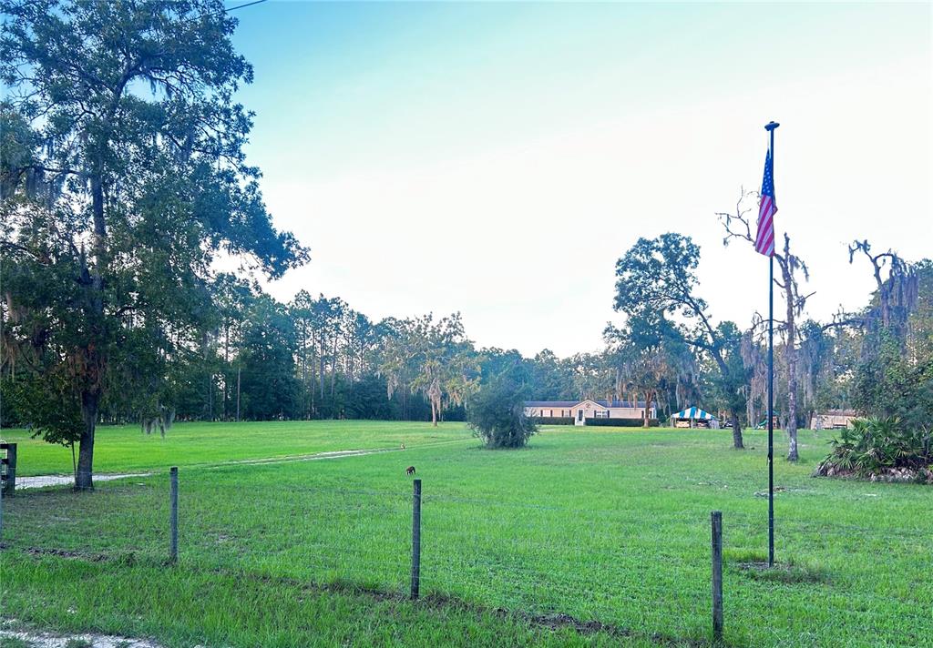 A large grassy field features a house in the distance and an American flag pole — 3560 NE 71ST AVENUE, HIGH SPRINGS, FL