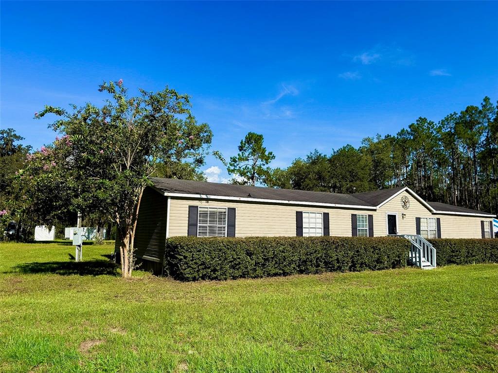 A single-story manufactured home with tan siding and a dark roof sits on a grassy lot — 3560 NE 71ST AVENUE, HIGH SPRINGS, FL