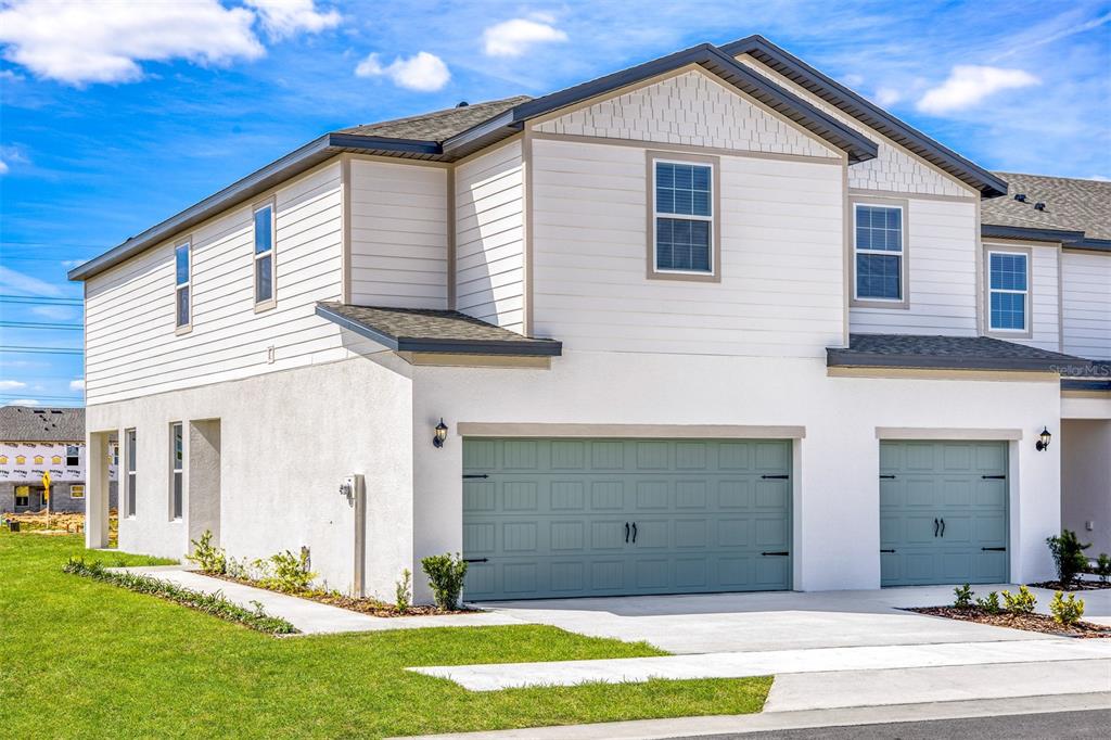 A two-story townhouse exterior features white siding, stucco walls, and two sage green garage doors — 643 POPPY LANE, DUNDEE, FL