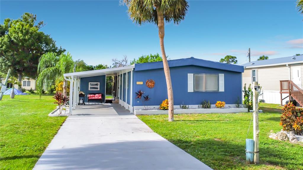 A blue mobile home features a concrete driveway, a covered carport, and a palm tree — 8207 ARCHIE STREET, ENGLEWOOD, FL
