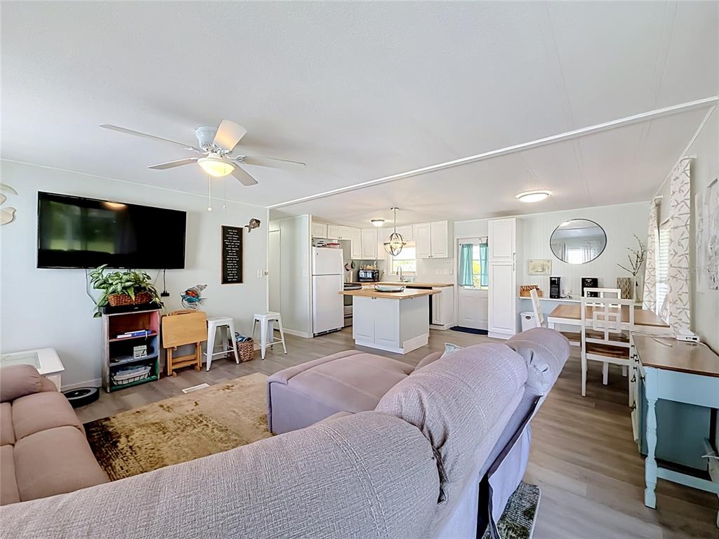 An open-concept living room and kitchen featuring light wood flooring, white cabinetry, and a sectional — 8207 ARCHIE STREET, ENGLEWOOD, FL