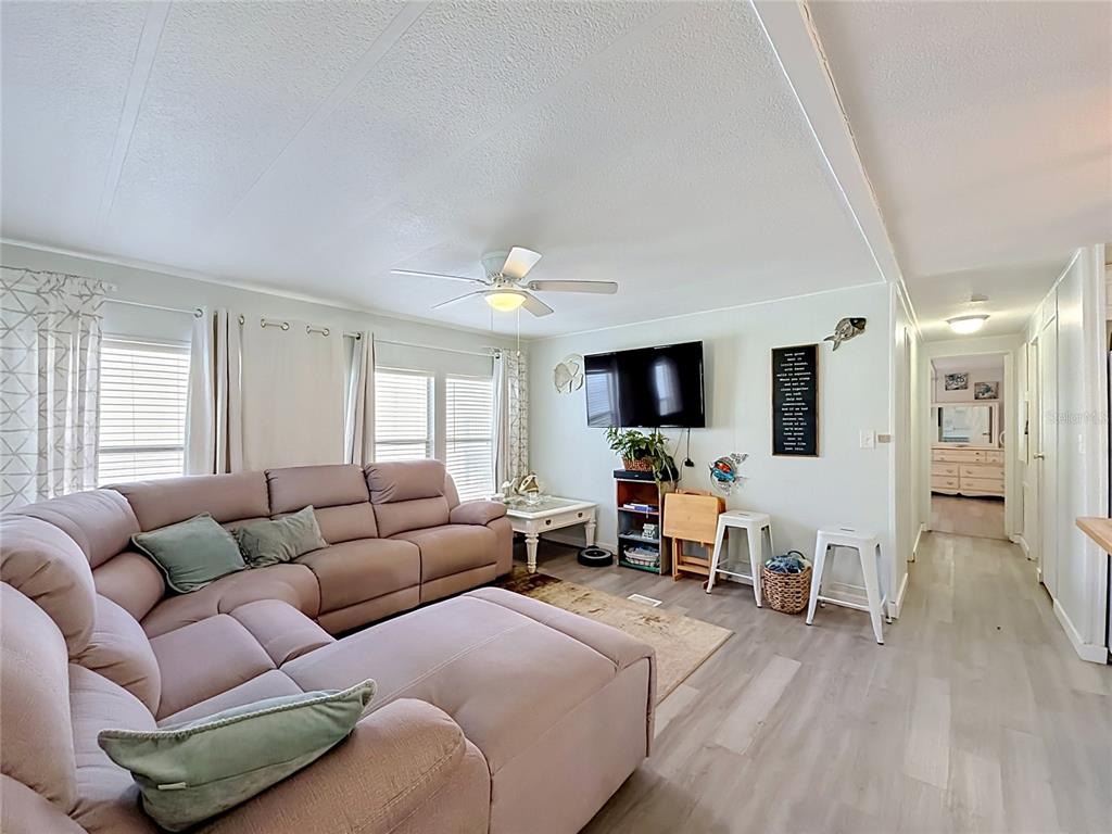 A living room features a large sectional sofa, a wall-mounted television, and light wood flooring — 8207 ARCHIE STREET, ENGLEWOOD, FL