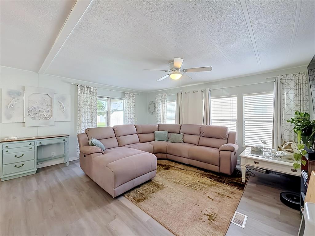 A living room features a large sectional sofa, a patterned area rug, and light-colored flooring — 8207 ARCHIE STREET, ENGLEWOOD, FL