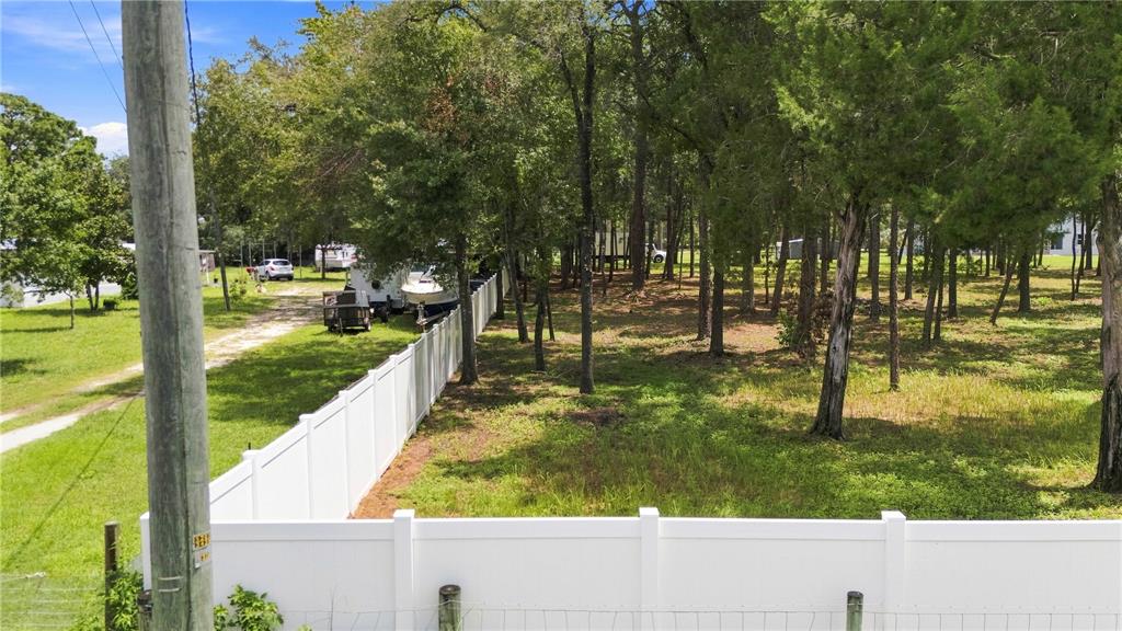 A white vinyl fence separates a grassy yard from a wooded lot with a boat trailer — 0 HIGHGROVE ROAD, SPRING HILL, FL