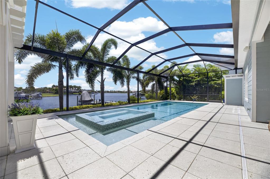 A screened-in patio features a rectangular swimming pool with an integrated spa overlooking a canal — 825 MANNS HARBOR DRIVE, APOLLO BEACH, FL