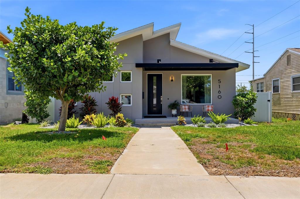 The exterior of a modern home features a covered porch with two chairs and landscaping — 5160 DARTMOUTH AVENUE N, ST PETERSBURG, FL