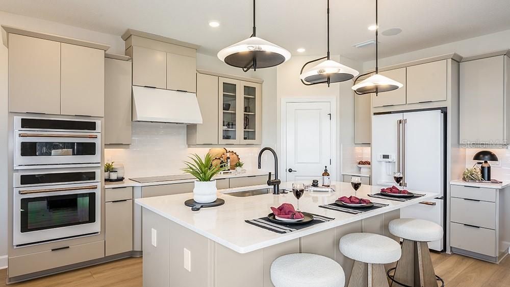 A modern kitchen features light-toned cabinetry, a central island with bar seating, and pendant lighting — 17806 SEDONA STREET, WINTER GARDEN, FL