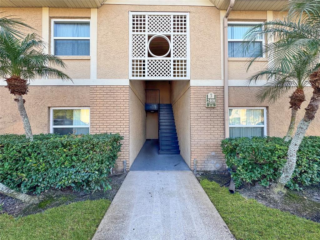 A concrete walkway leads to an exterior staircase between two sections of a tan building — 2408 BARLEY CLUB COURT UNIT 2, ORLANDO, FL