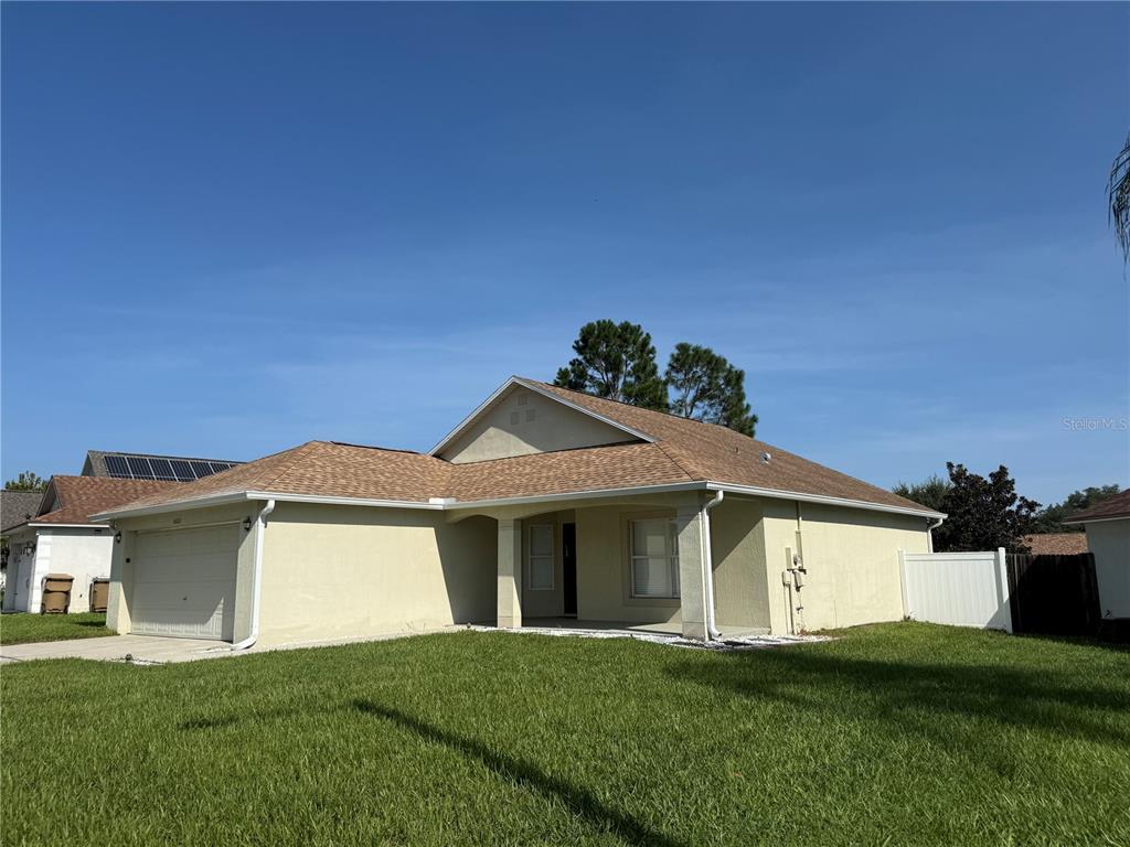 A single-story house with a tan stucco exterior, a two-car garage, and a shingled roof — 16212 COOPERS HAWK AVENUE, CLERMONT, FL