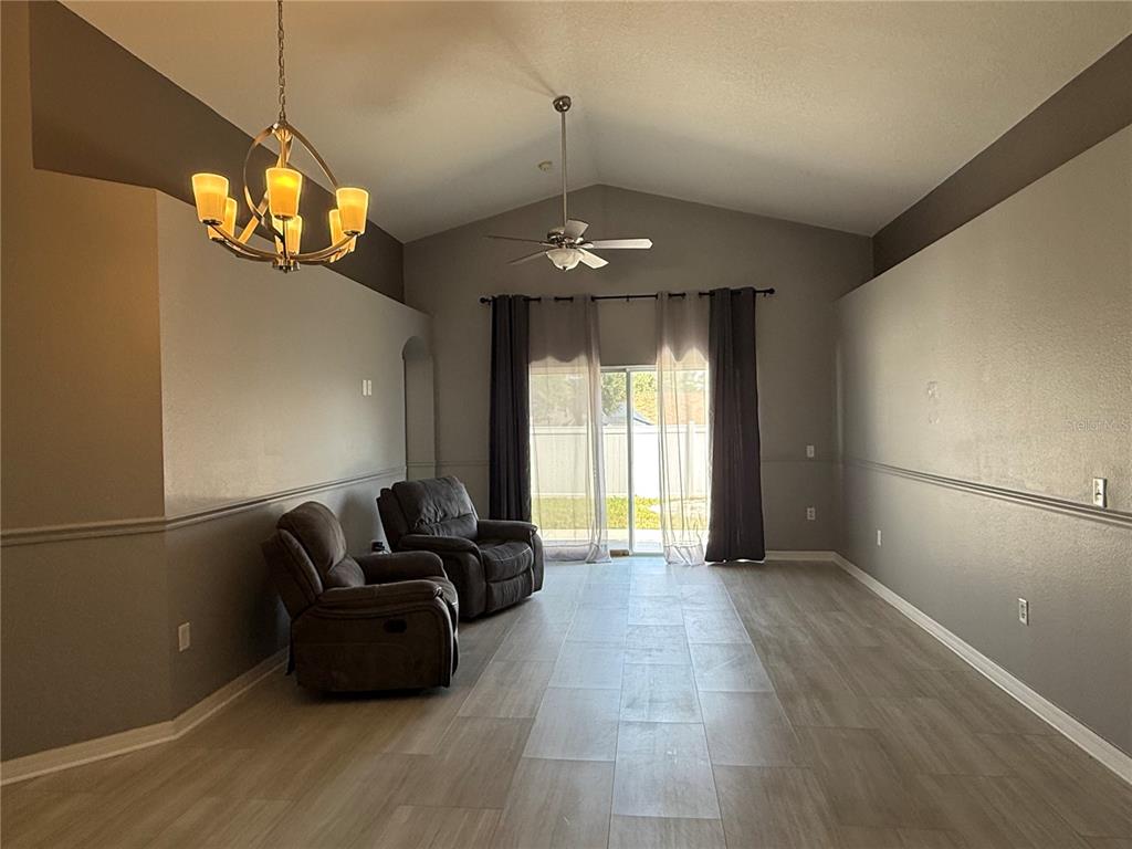 A living room features gray walls, tile flooring, a vaulted ceiling, and two brown recliners — 16212 COOPERS HAWK AVENUE, CLERMONT, FL