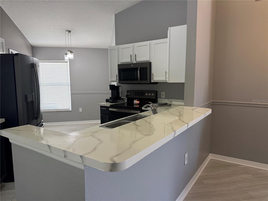 A kitchen features white cabinets, a marble-patterned breakfast bar, and stainless steel appliances — 16212 COOPERS HAWK AVENUE, CLERMONT, FL