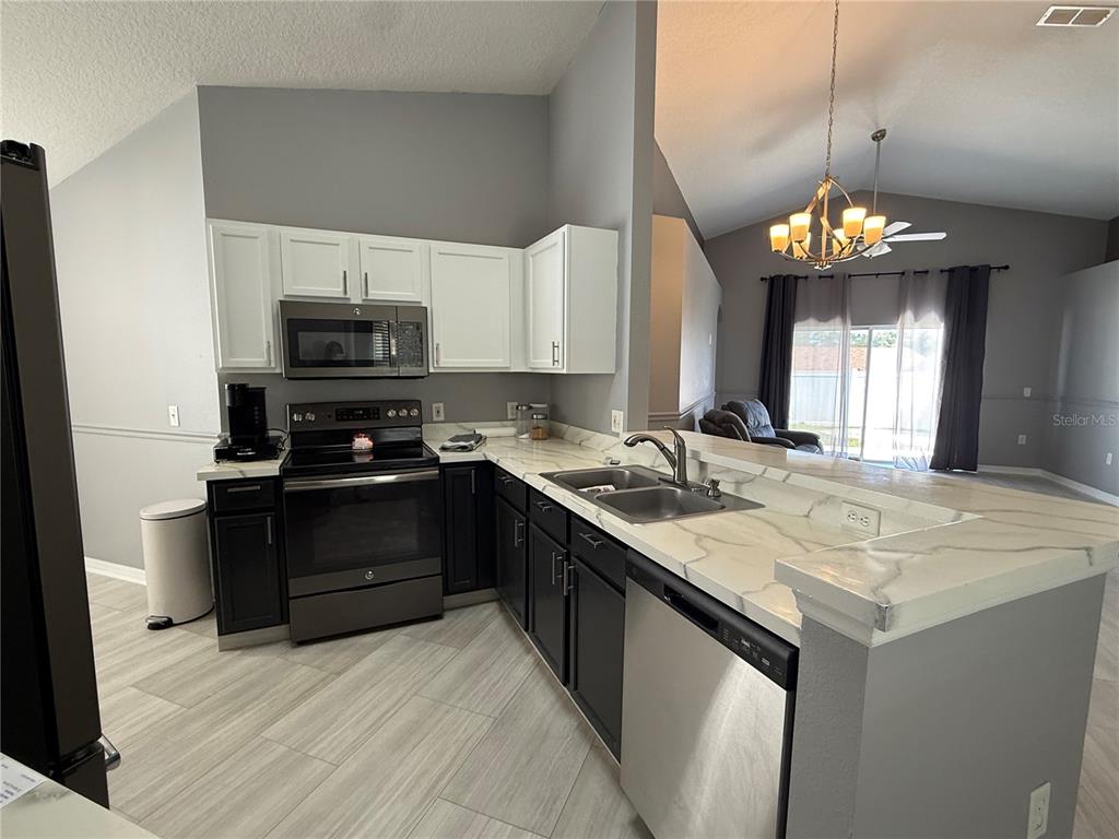 A kitchen features white upper cabinets, dark lower cabinets, marble-look countertops, and stainless steel appliances — 16212 COOPERS HAWK AVENUE, CLERMONT, FL