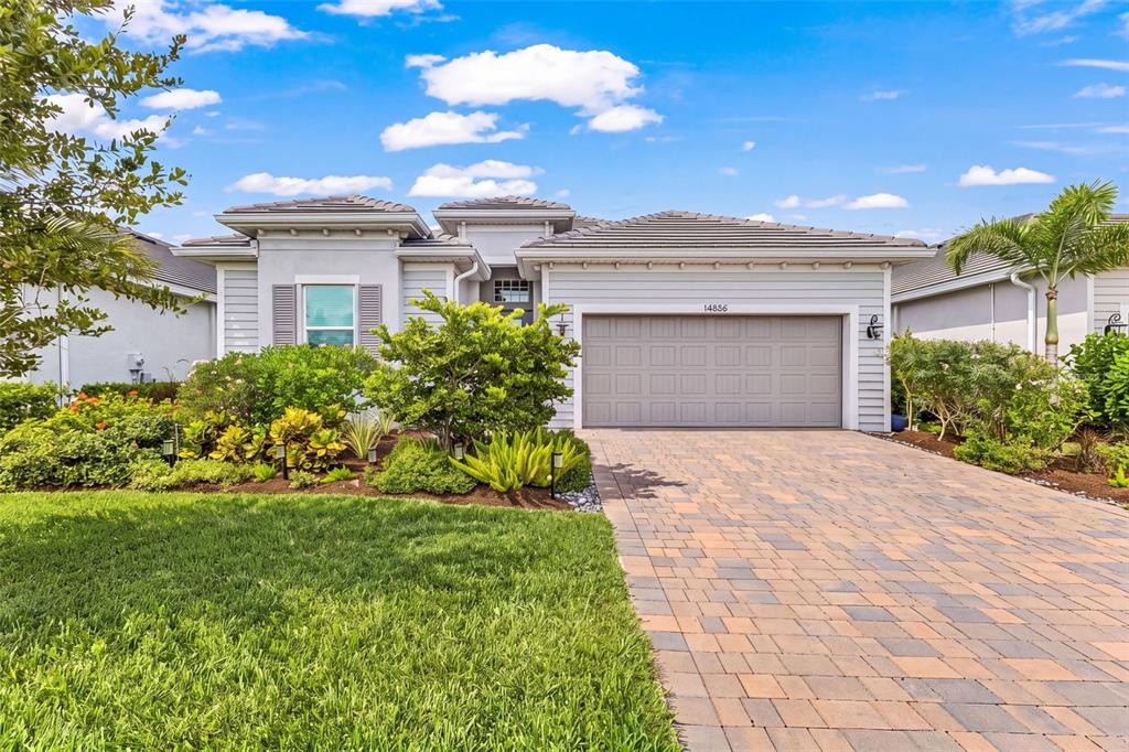 A single-story house with a gray garage, a paver driveway, and landscaped front yard — 14856 REDBUD LANE, PUNTA GORDA, FL