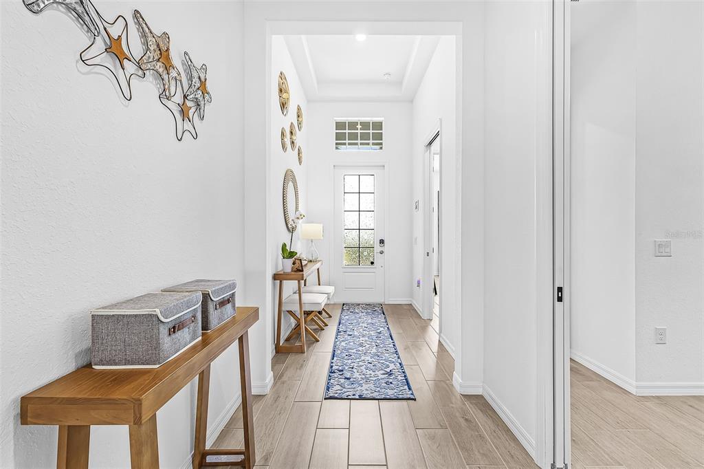A bright entryway features light wood-look tile flooring, a console table, and a glass-paneled front door — 14856 REDBUD LANE, PUNTA GORDA, FL