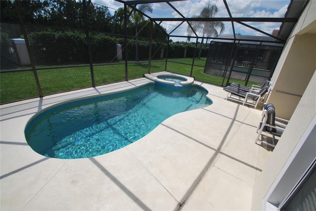 A screened-in patio features a kidney-shaped swimming pool with an attached spa and lounge chairs — 217 ROBIN ROAD, DAVENPORT, FL