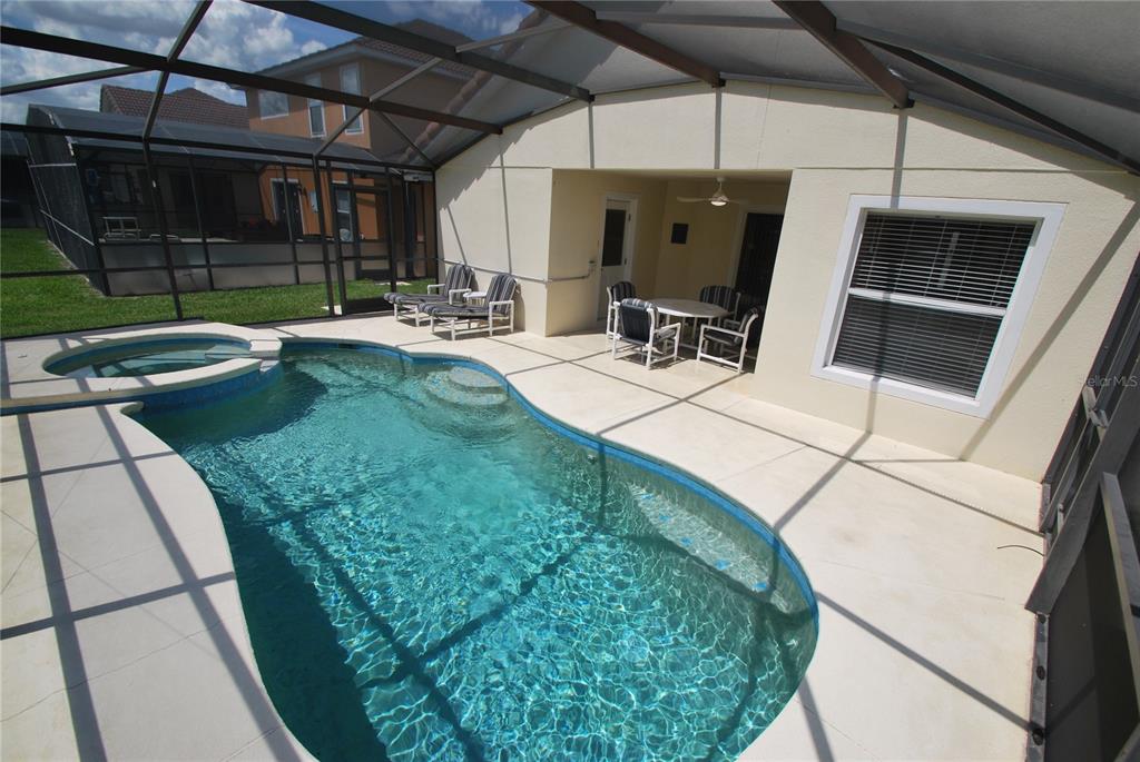 A swimming pool and spa are enclosed within a screened lanai with patio furniture — 217 ROBIN ROAD, DAVENPORT, FL