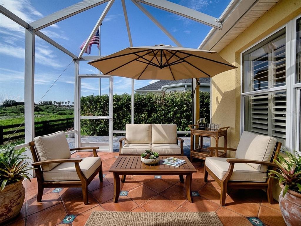A screened-in patio features outdoor furniture, a tan umbrella, and tile flooring overlooking a yard — 622 MAYBANK LOOP, THE VILLAGES, FL