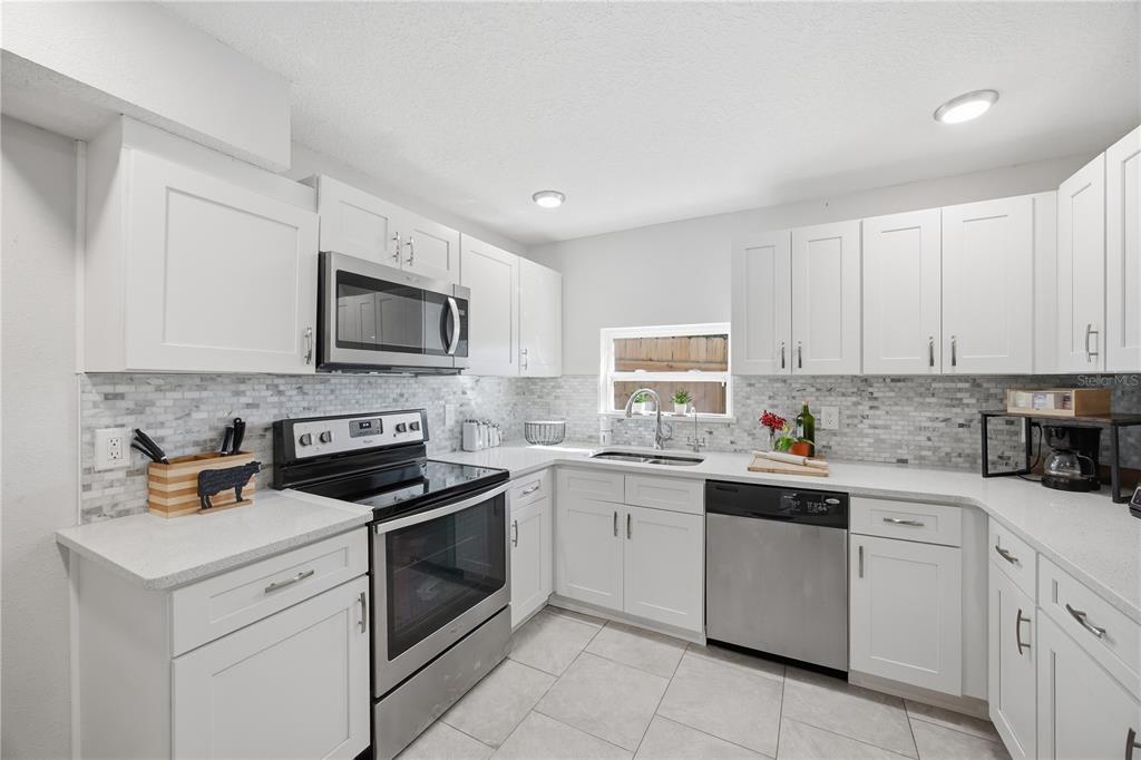 A kitchen with white cabinets, stainless steel appliances, and a light-colored tiled backsplash — 2350 VALLEY DRIVE, APOPKA, FL