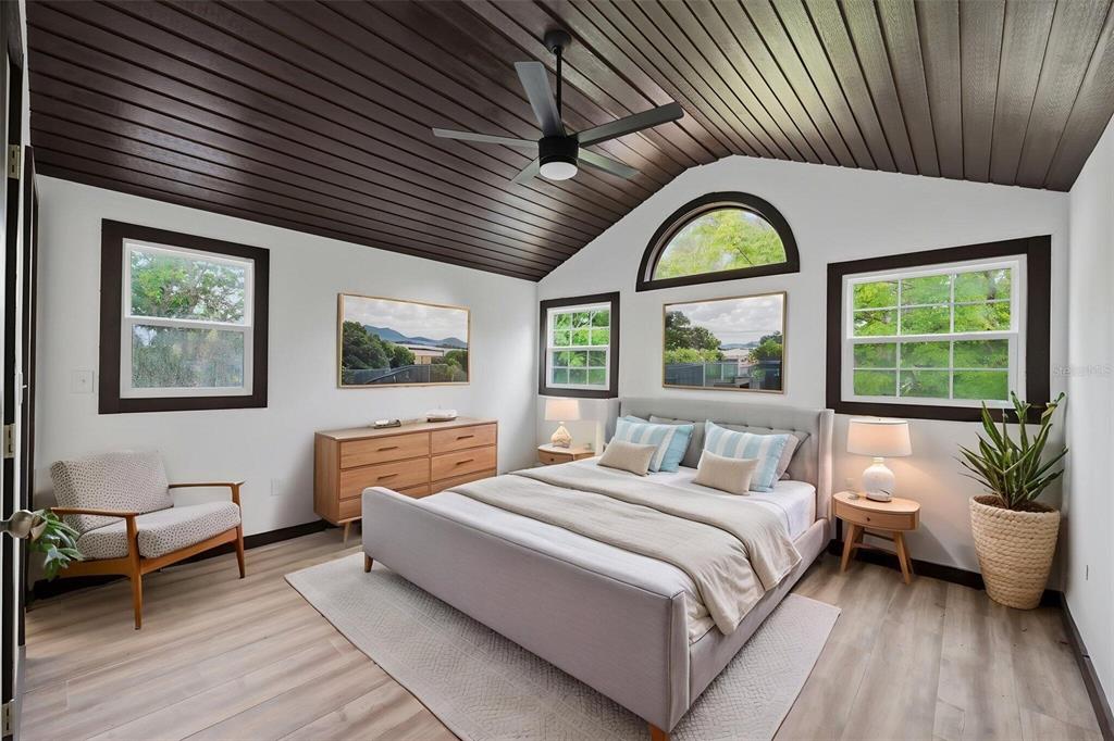 A bedroom features a dark wood-paneled vaulted ceiling, light wood flooring, and a gray bed — 15017 DAYTON DRIVE, HUDSON, FL