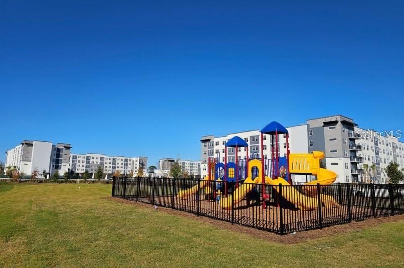A playground with yellow slides sits inside a fenced area in front of apartment buildings — 5579 MILLENIA BOULEVARD UNIT 515, ORLANDO, FL