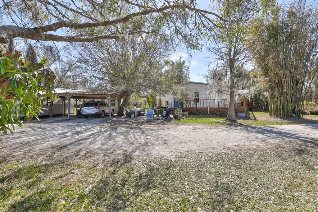 A house with a carport and a wooden deck sits on a sandy lot — 20112 HOBBS ROAD, WIMAUMA, FL