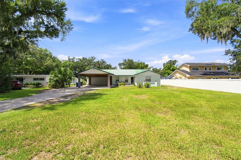 A single-story house with a carport and a large front lawn under a blue sky — 2219 NEW JERSEY RD, LAKELAND, FL