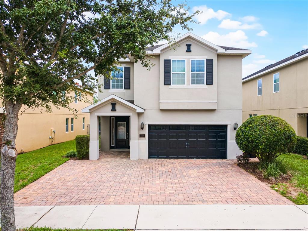 A two-story house with a beige stucco exterior, black garage door, and a brick paver driveway — 7513 MARKER AVENUE, KISSIMMEE, FL