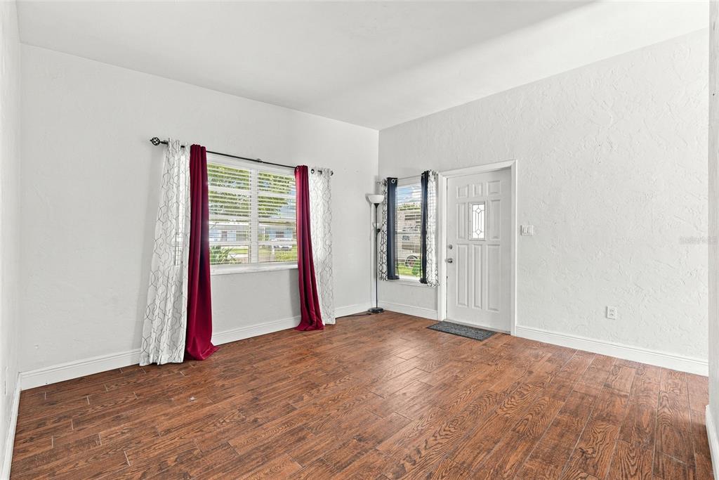 An empty room features white walls, wood-look tile flooring, two windows with curtains, and a door — 10594 104TH AVENUE, LARGO, FL