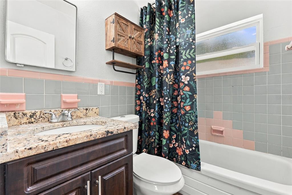 A bathroom features a dark wood vanity, granite countertop, floral shower curtain, and vintage tile — 10594 104TH AVENUE, LARGO, FL
