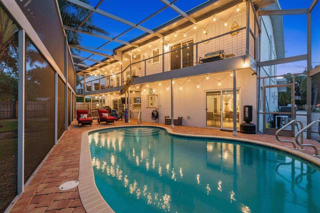 A two-story house with a screened-in pool, brick patio, and string lights at dusk — 201 LAGOON DRIVE, PALM HARBOR, FL