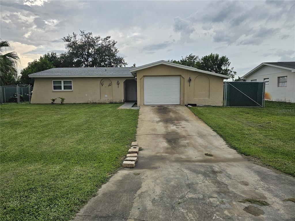 A single-story house with a beige stucco exterior, a one-car garage, and a concrete driveway — 1706 MARGATE BOULEVARD, LEHIGH ACRES, FL