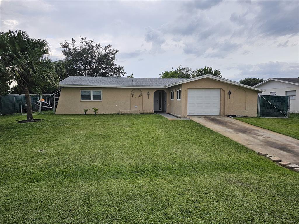A single-story tan house with a white garage door and a large front lawn — 1706 MARGATE BOULEVARD, LEHIGH ACRES, FL