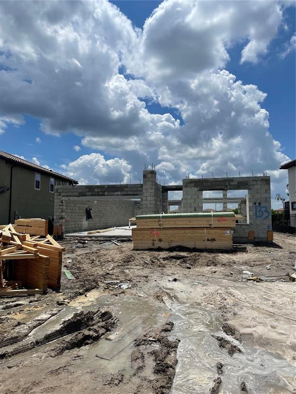 A construction site shows a concrete block structure with stacked lumber under a cloudy sky — 8530 DOVE BOG TERRACE, PARRISH, FL