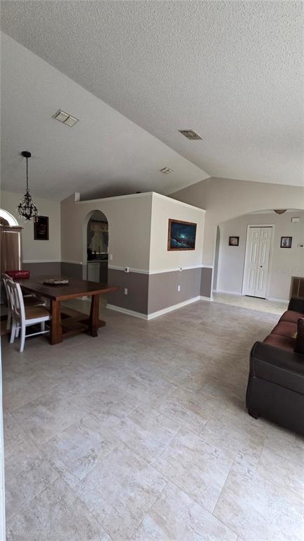 An open-concept living and dining area features vaulted ceilings, tile flooring, and arched wall openings — 36 BRADFORD COURT, KISSIMMEE, FL