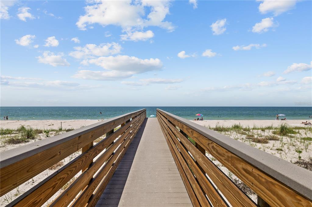 A wooden boardwalk leads through sand dunes toward a beach under a blue sky — 555 GULF WAY UNIT 6S, ST PETE BEACH, FL