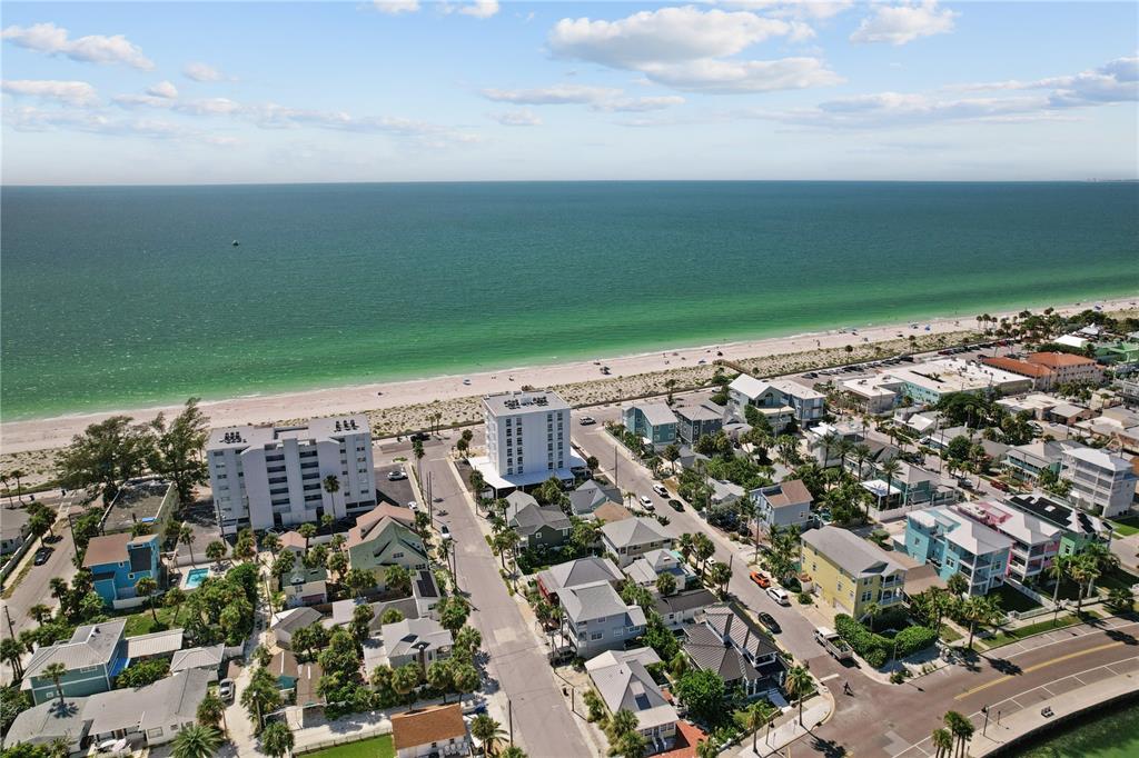 An aerial view shows a coastal neighborhood with houses, apartment buildings, and a sandy beach — 555 GULF WAY UNIT 6S, ST PETE BEACH, FL