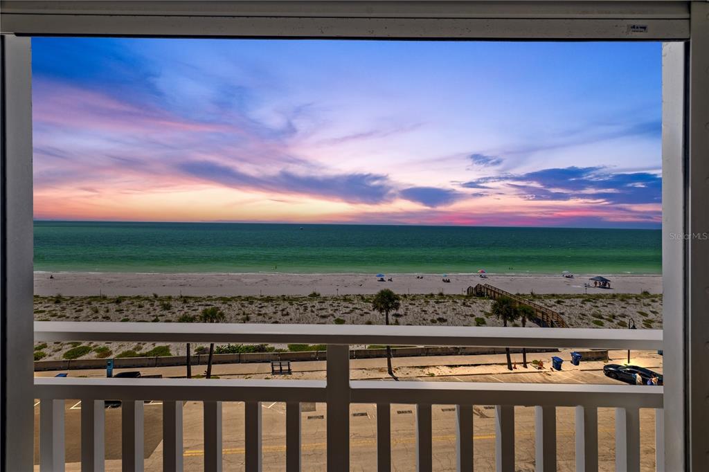 A balcony view overlooks a sandy beach, the ocean, and a sunset sky — 555 GULF WAY UNIT 6S, ST PETE BEACH, FL