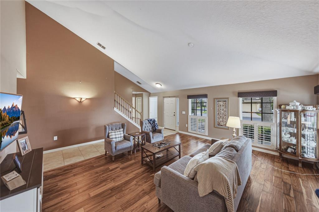 A living room features wood-look flooring, a vaulted ceiling, and a staircase with railings — 2024 LARKSPUR COURT, TRINITY, FL