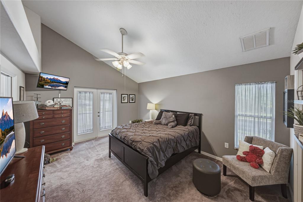 A bedroom features a vaulted ceiling, a dark wood bed frame, and a ceiling fan — 2024 LARKSPUR COURT, TRINITY, FL