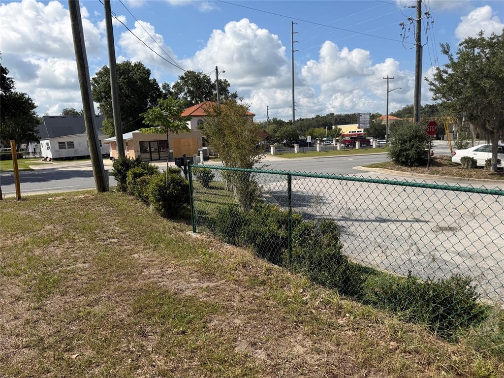 A chain-link fence borders a grassy lot near a street intersection with a stop sign — 121 W LEMON STREET, LADY LAKE, FL